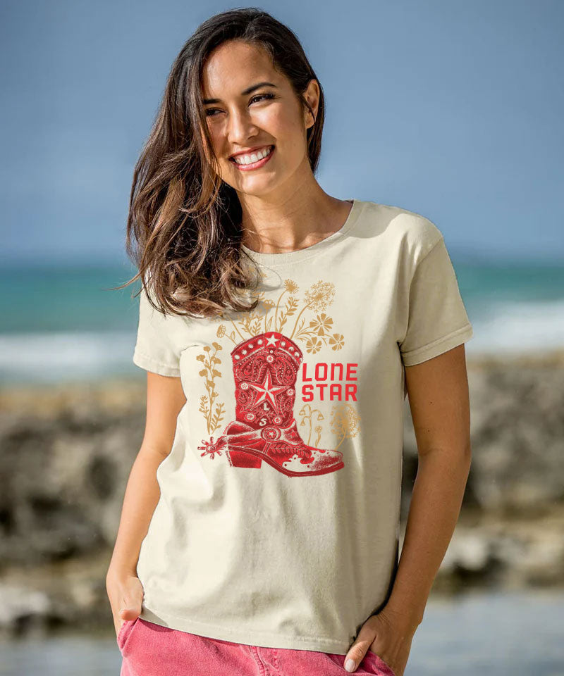 Woman wearing a white t-shirt with a red boot design and 'Lone Star' text, standing on a beach.