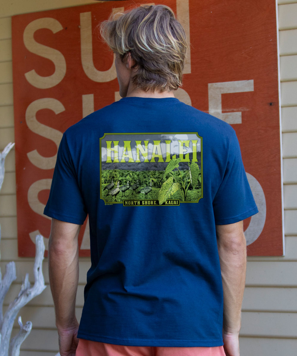 Man wearing a blue t-shirt with 'Hanalei' graphic on the back, standing in front of a red sign. View 2