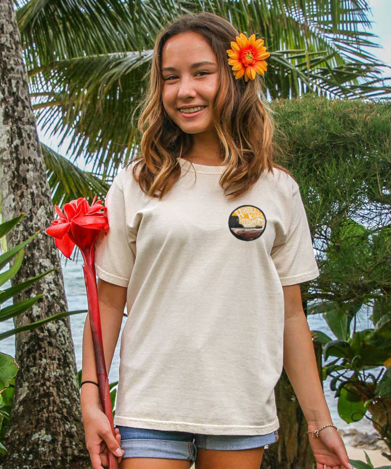 Woman wearing a t-shirt with a circular design, standing outdoors with palm trees in the background View 3