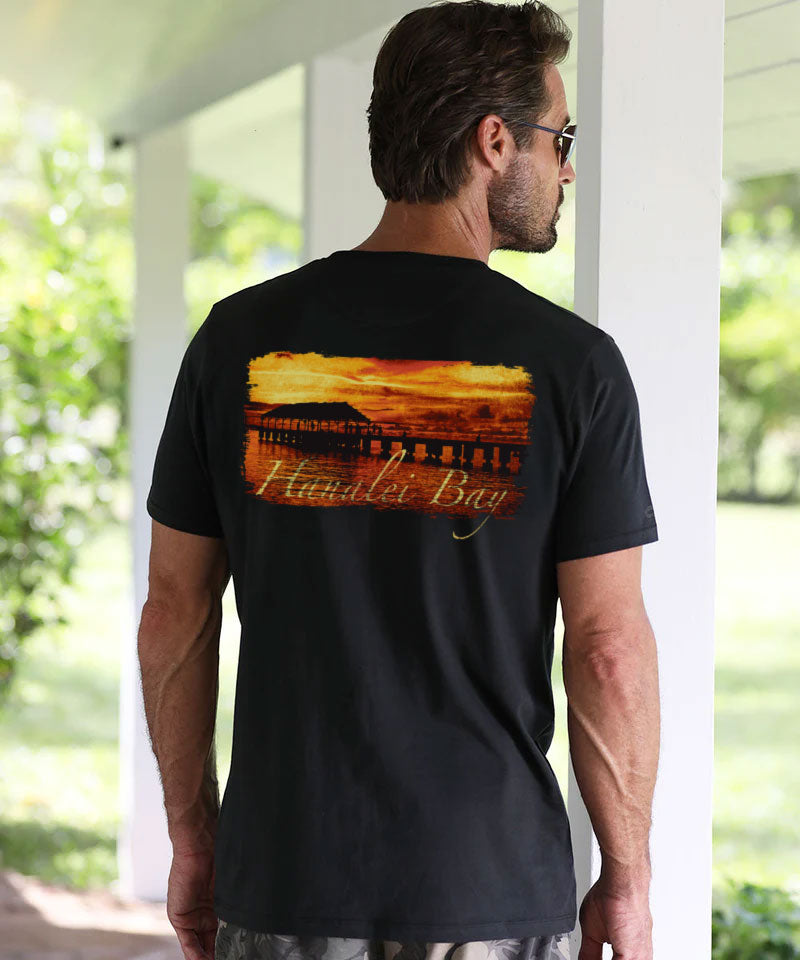 Man wearing a black t-shirt with a sunset design and text, standing on a porch. View 2