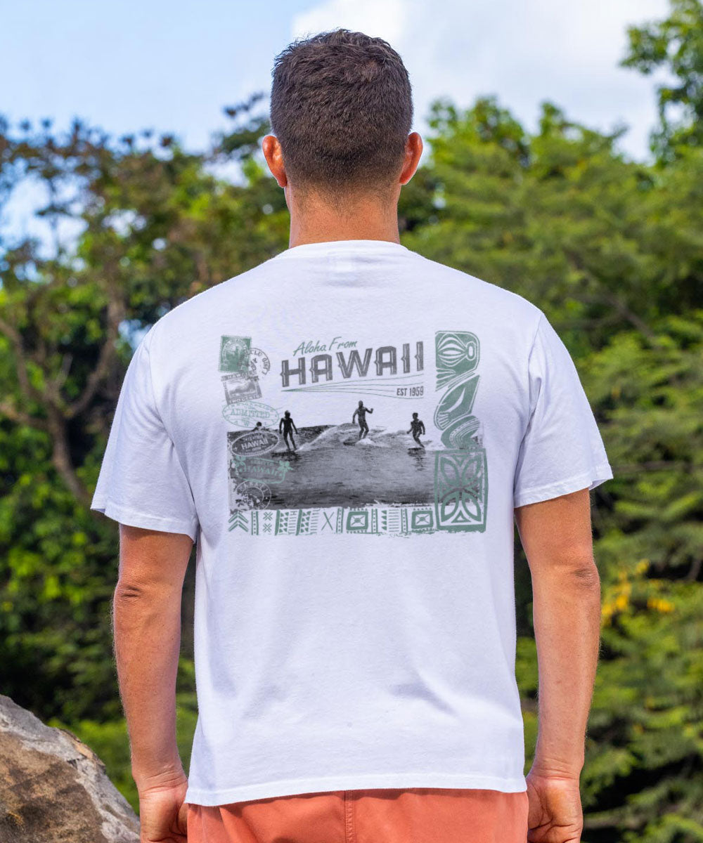 Man wearing a white t-shirt with a graphic design of people surfing on the back, standing outdoors. View 2