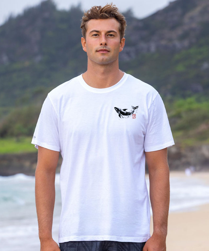 Man in a white t-shirt with a small whale design, standing on a beach View 3