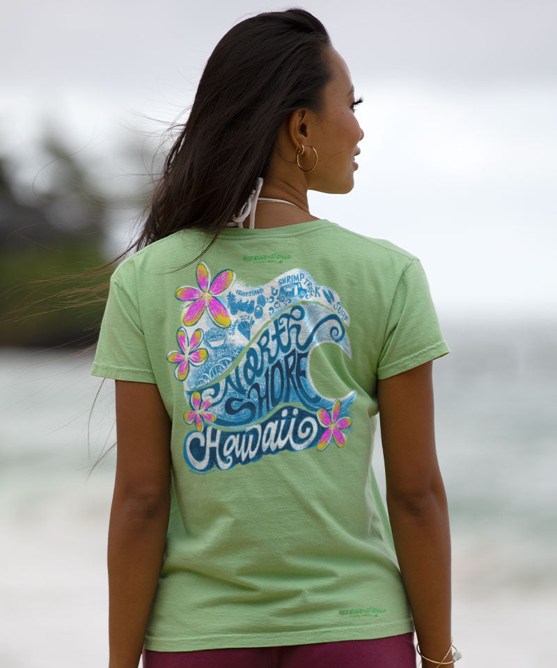 Woman wearing a green t-shirt with floral and wave design, standing outdoors. View 3