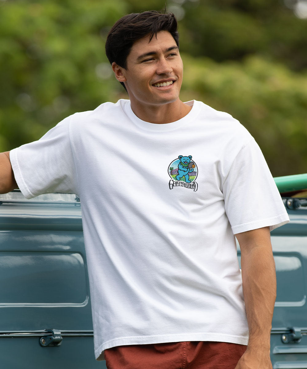 Man wearing a white t-shirt with a graphic design, standing next to a vehicle outdoors. View 3