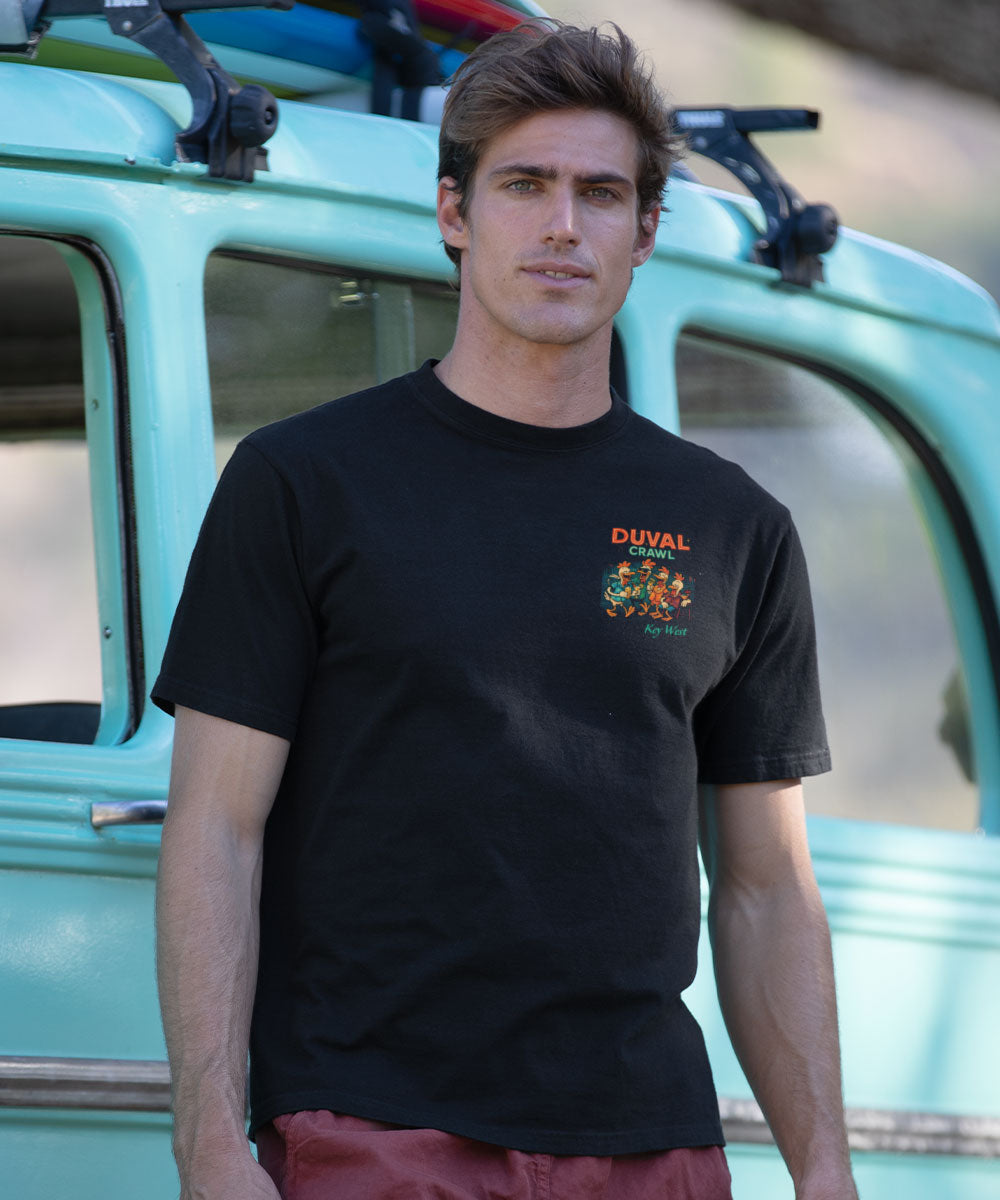 Man wearing a black t-shirt with a logo standing in front of a vintage vehicle View 3