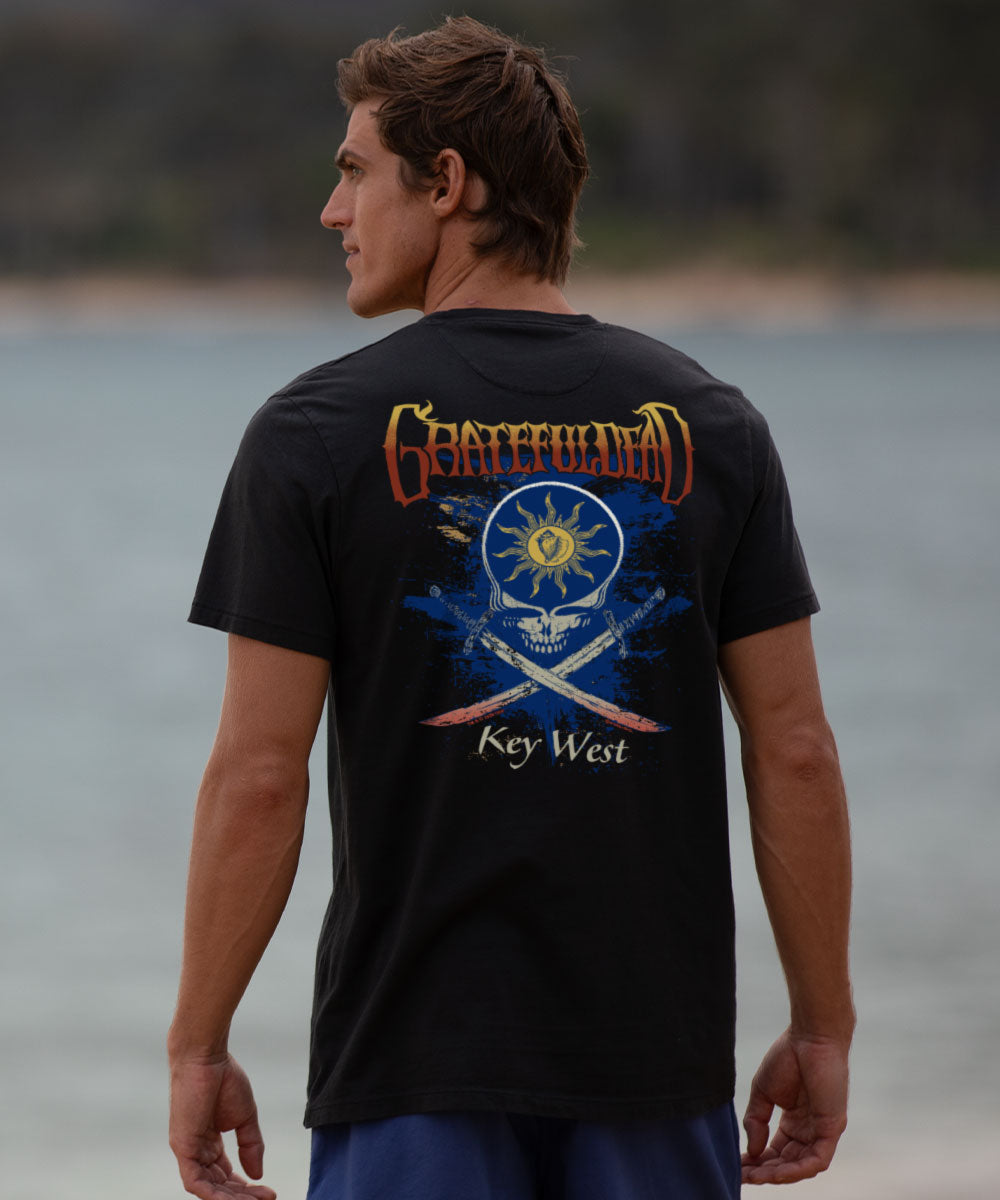 Man wearing a black t-shirt with a graphic design standing by a body of water. View 2