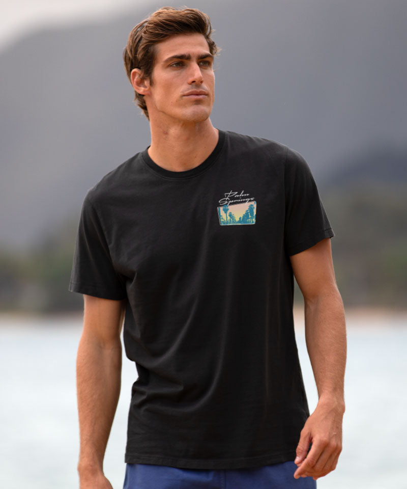 Man wearing a black t-shirt with a small graphic on a blurred natural background View 3
