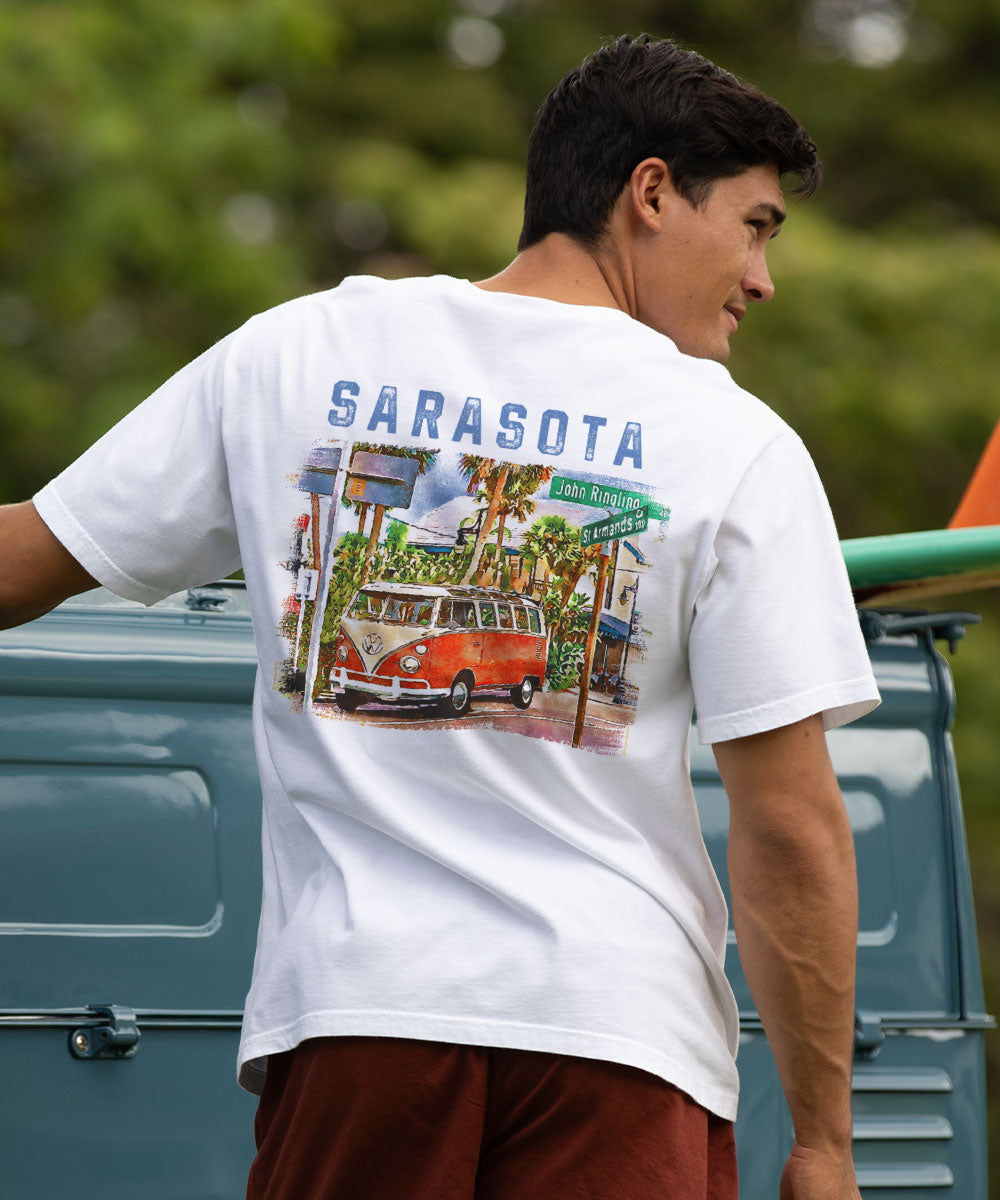 Man wearing a white t-shirt with a graphic design and 'Sarasota' text, standing next to a vintage van. View 2