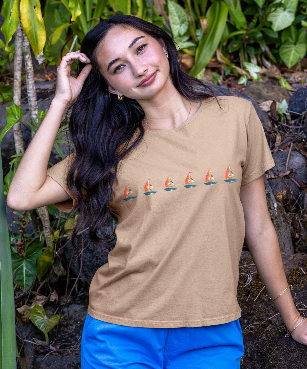 Woman wearing a beige t-shirt with a graphic design, standing in a natural setting. View 2