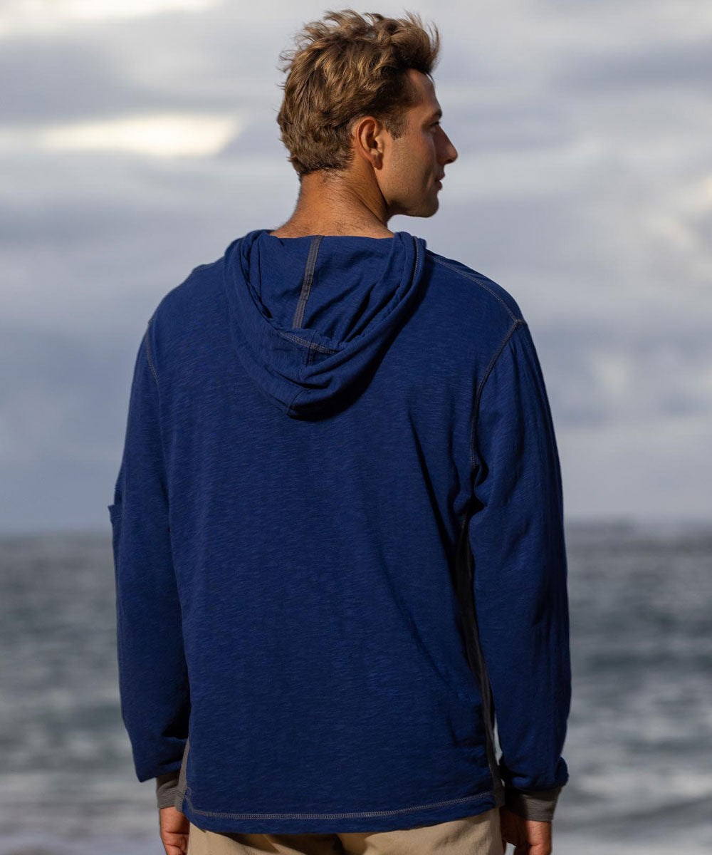 Person wearing a blue hoodie standing by the ocean with a cloudy sky. View 3