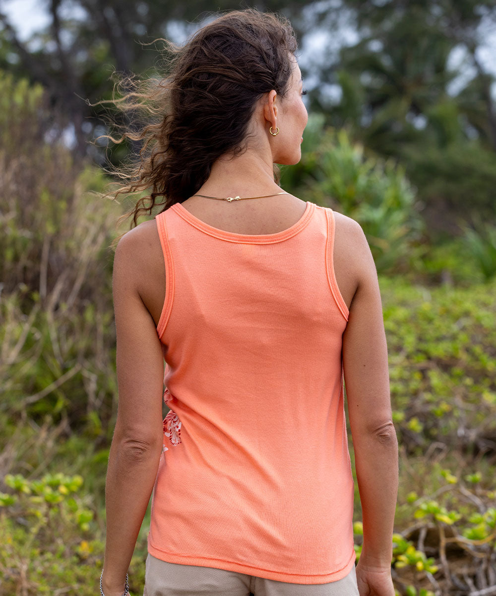 Woman wearing a coral tank top standing in a natural setting with greenery. View 3