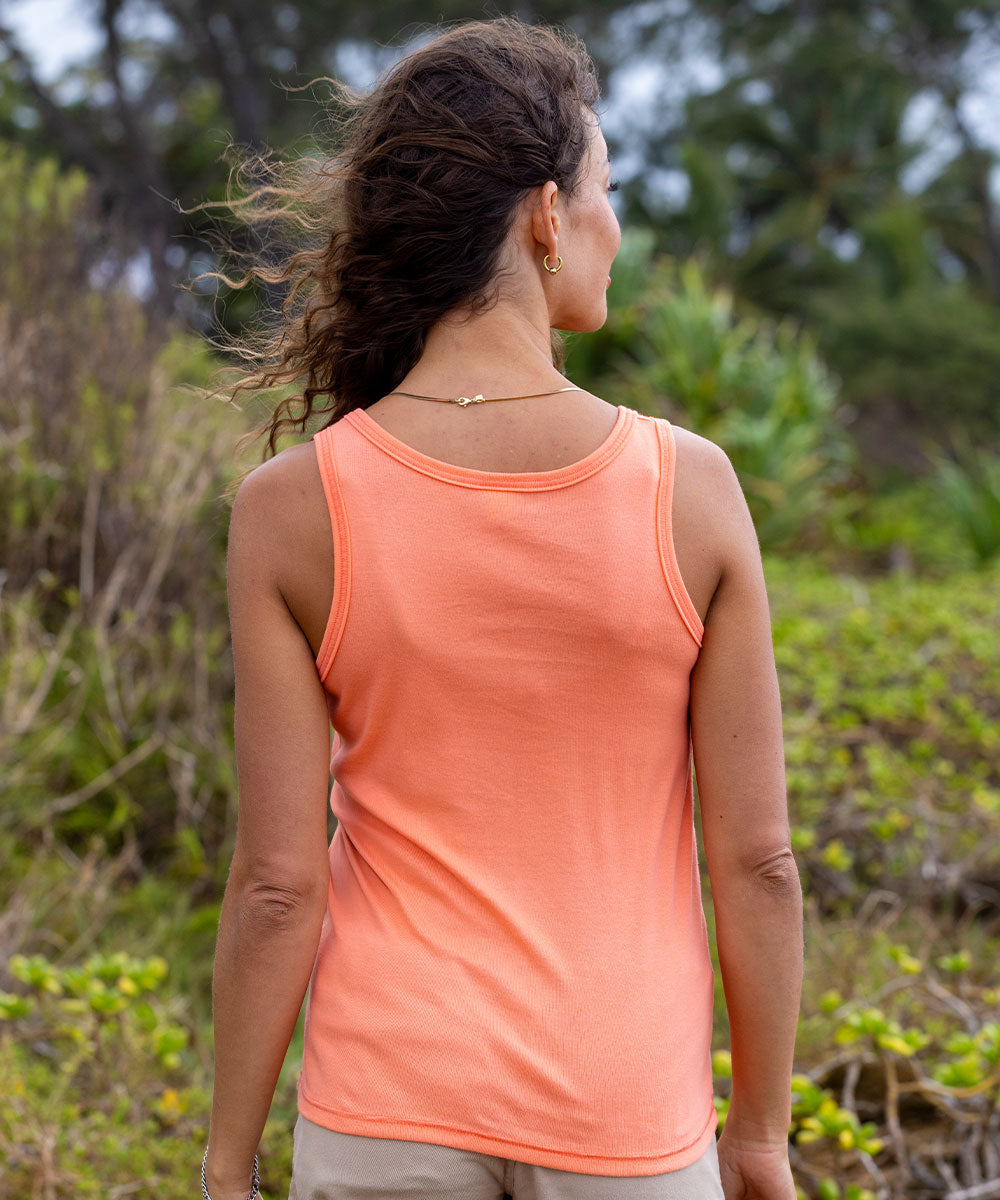 Woman wearing a coral tank top standing in a natural setting with greenery. View 3