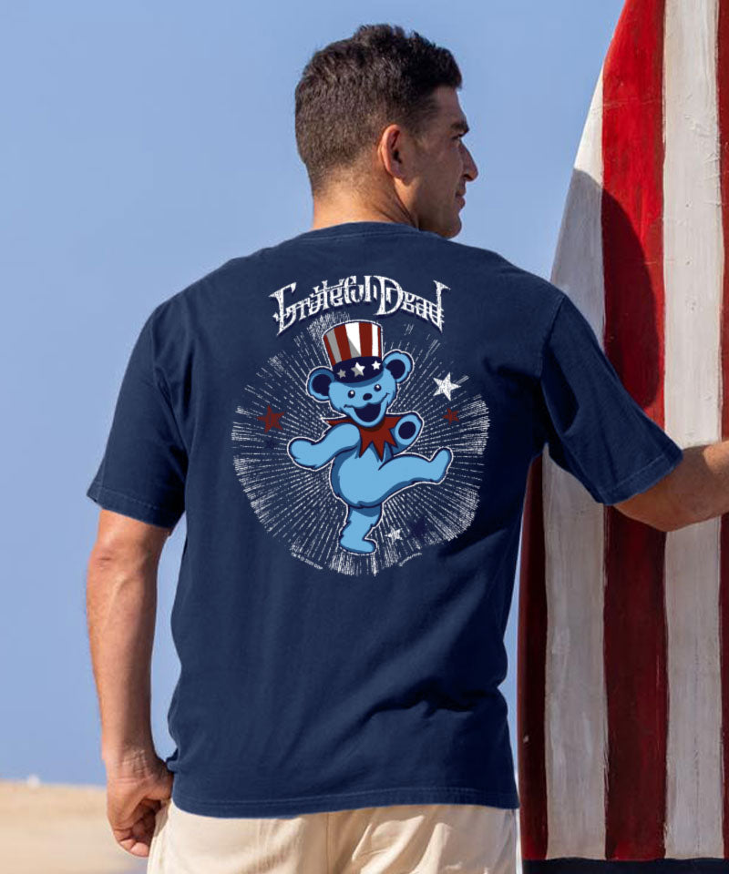 Man wearing a navy blue t-shirt with a graphic design, standing against a clear blue sky. View 2