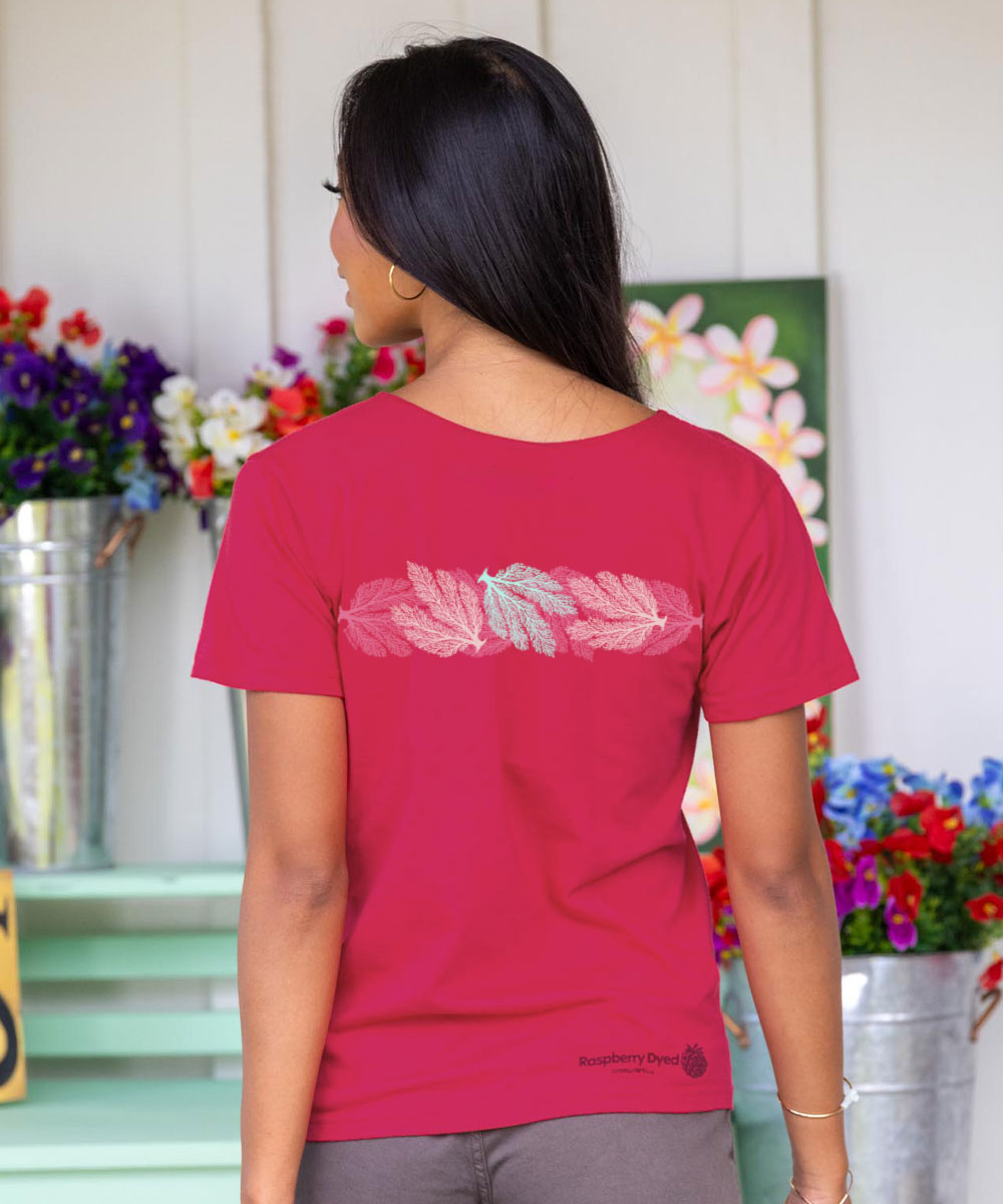 Woman wearing a raspberry dyed t-shirt with a design on the back, standing in front of floral arrangements. View 3