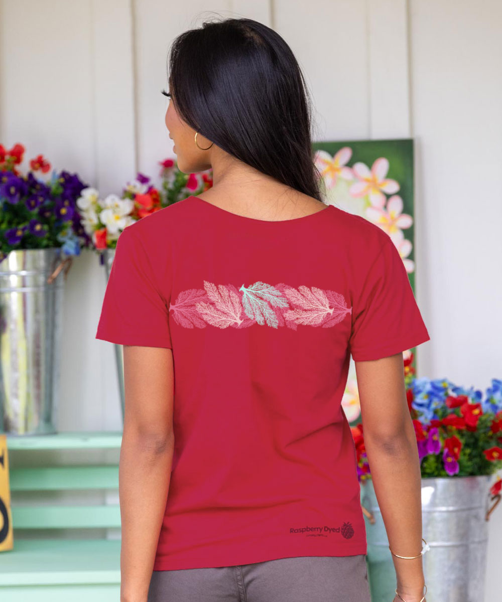 Woman wearing a raspberry dyed t-shirt with a design on the back, standing in front of floral arrangements. View 3