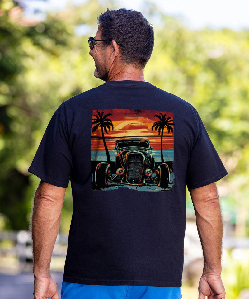Man wearing a black t-shirt with a graphic of a hot rod and palm trees on the back, standing outdoors. View 2