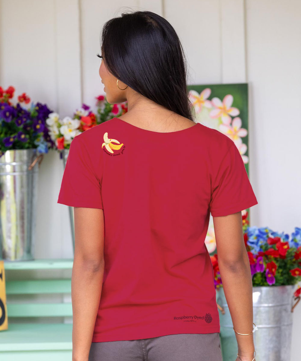Person wearing a raspberry dyed t-shirt with a logo, standing in front of floral arrangements. View 3