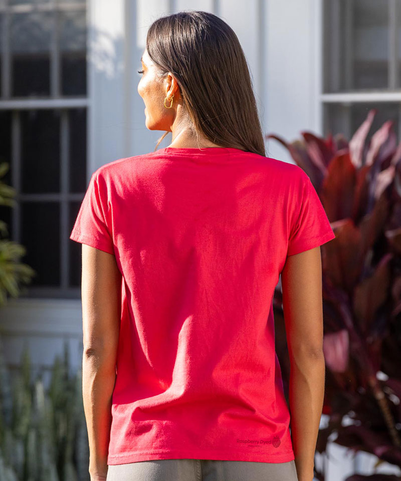 Person wearing a raspberry dyed t-shirt with a logo on the back, standing outdoors. View 3