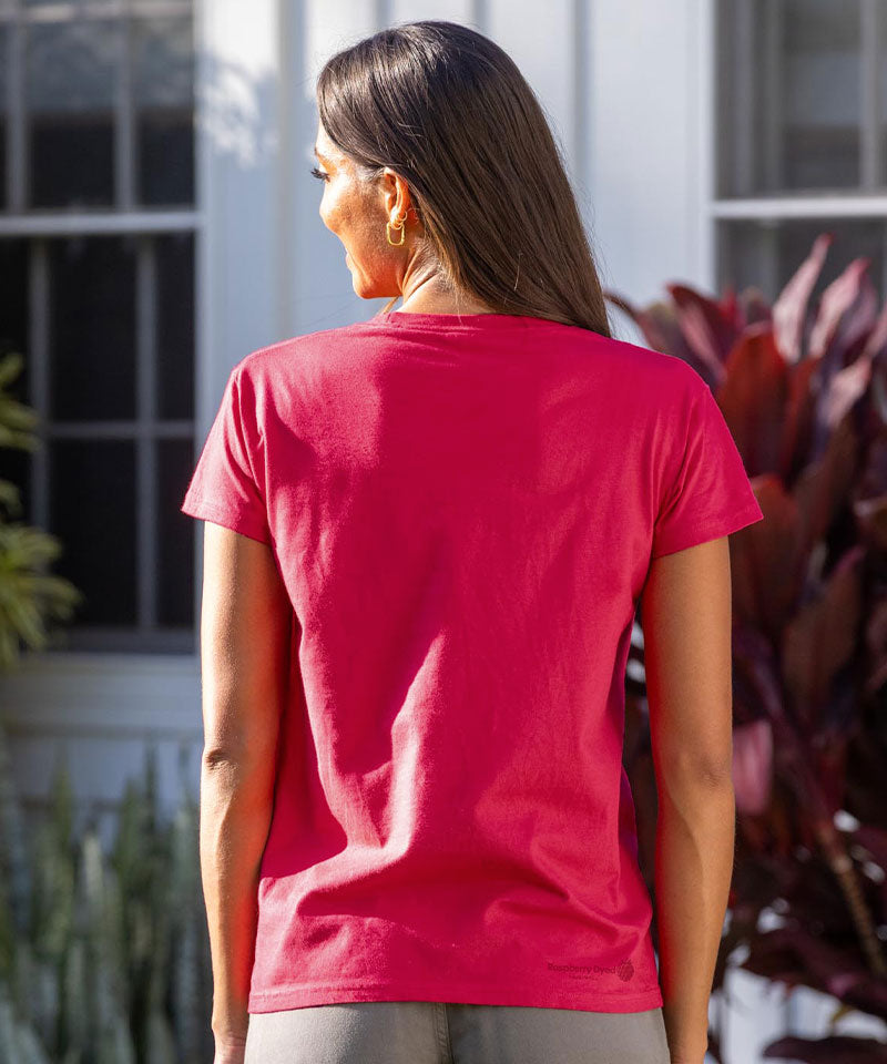 Person wearing a raspberry dyed t-shirt with a logo on the back, standing outdoors. View 3