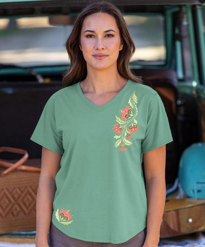 Woman wearing a green t-shirt with floral design in front of a vehicle. View 2