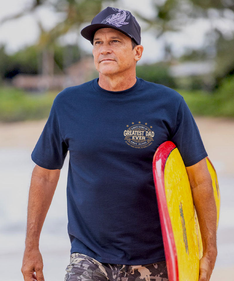 Man wearing a navy blue t-shirt with a logo, holding a red and yellow surfboard on a beach. View 3