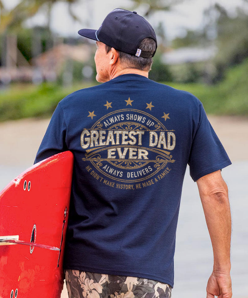 Man wearing a blue t-shirt with 'Greatest Dad Ever' text, holding a red surfboard.