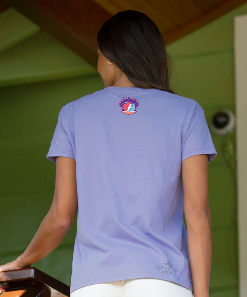 A woman viewed from behind wearing a light periwinkle blue t-shirt with a circular red, white, and blue crest graphic on the upper back, set against a green wall background. View 3