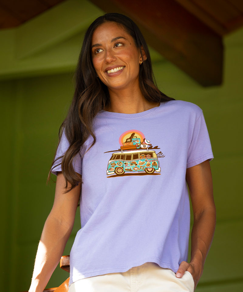 Woman wearing a purple t-shirt with a colorful graphic design, standing against a green background. View 2