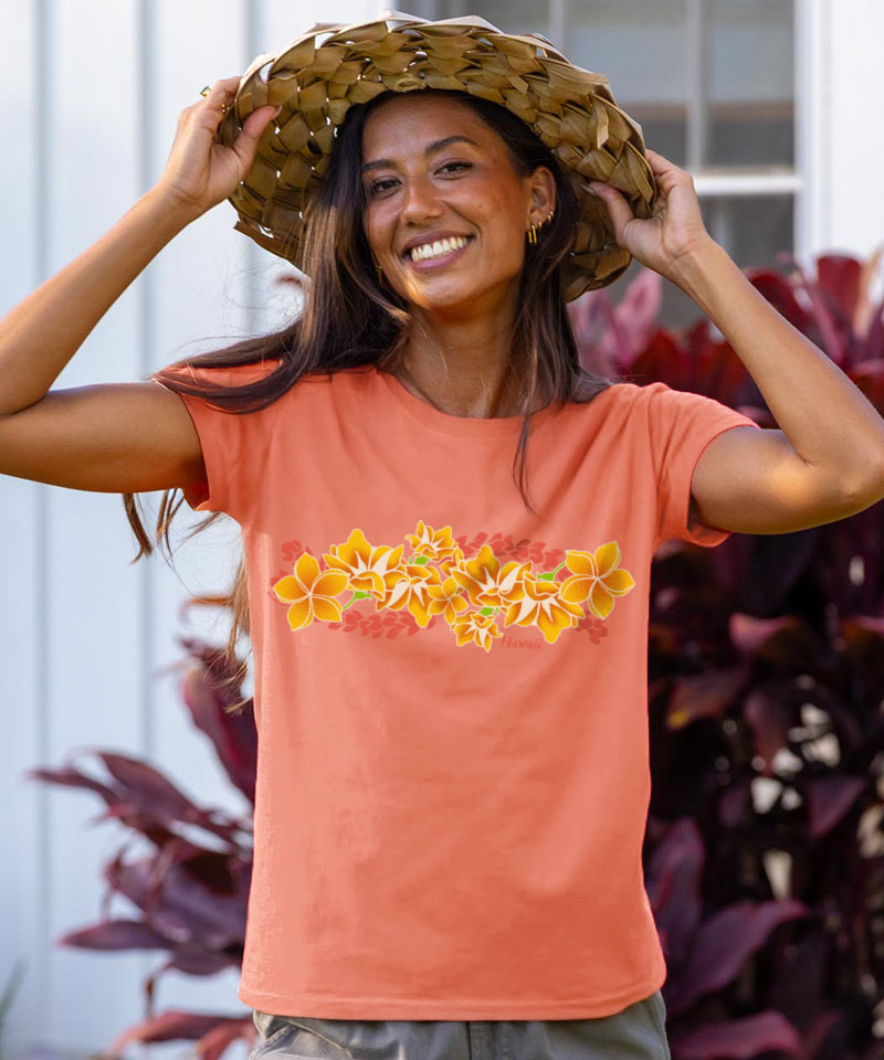 Woman wearing a coral t-shirt with floral design and a straw hat, standing outdoors. View 2