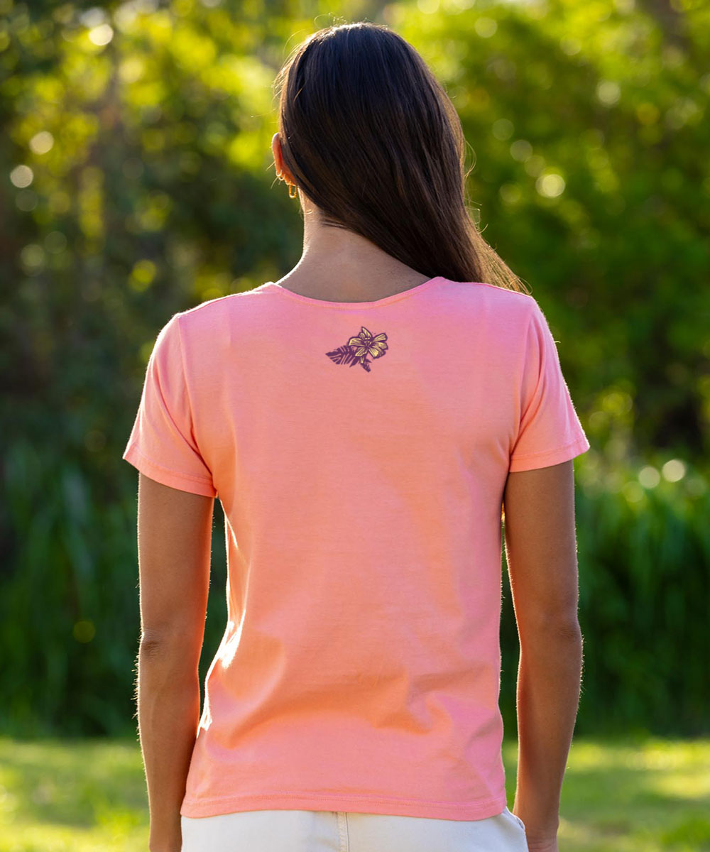 Person wearing a coral t-shirt with a logo on the back, standing outdoors. View 3