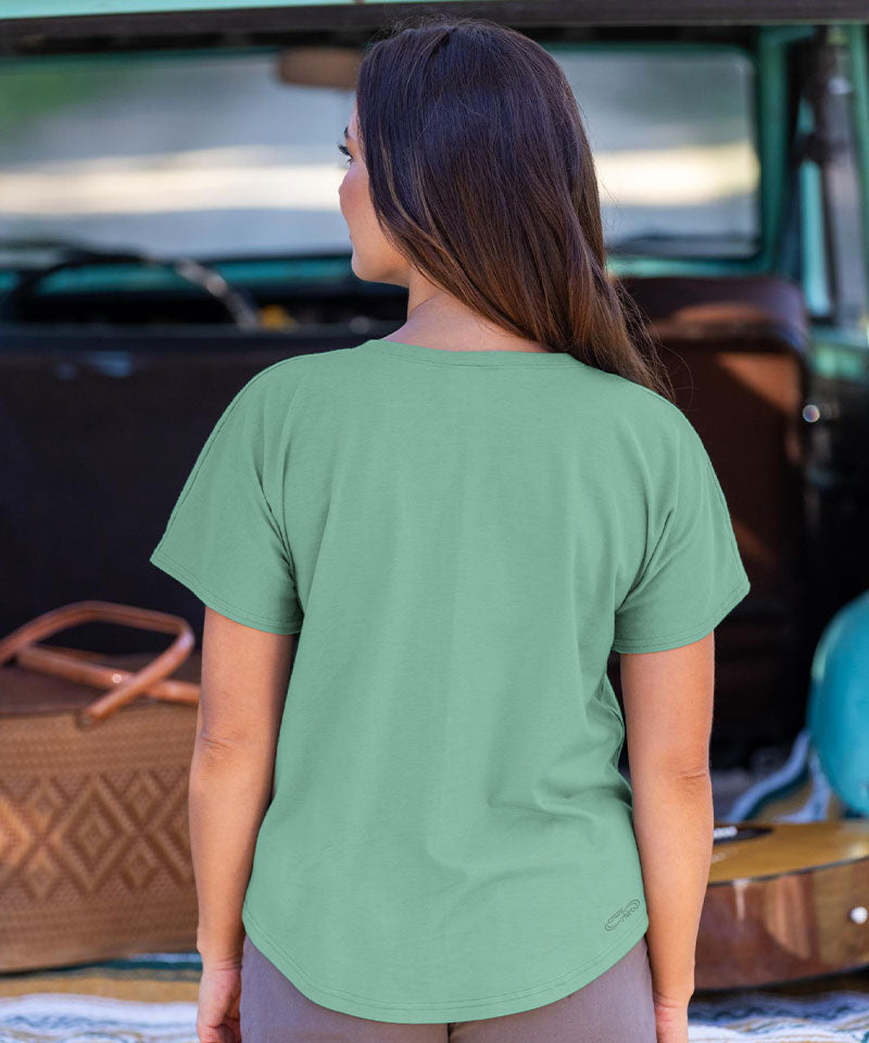 Woman wearing a green t-shirt with a logo, standing in front of a vehicle. View 3
