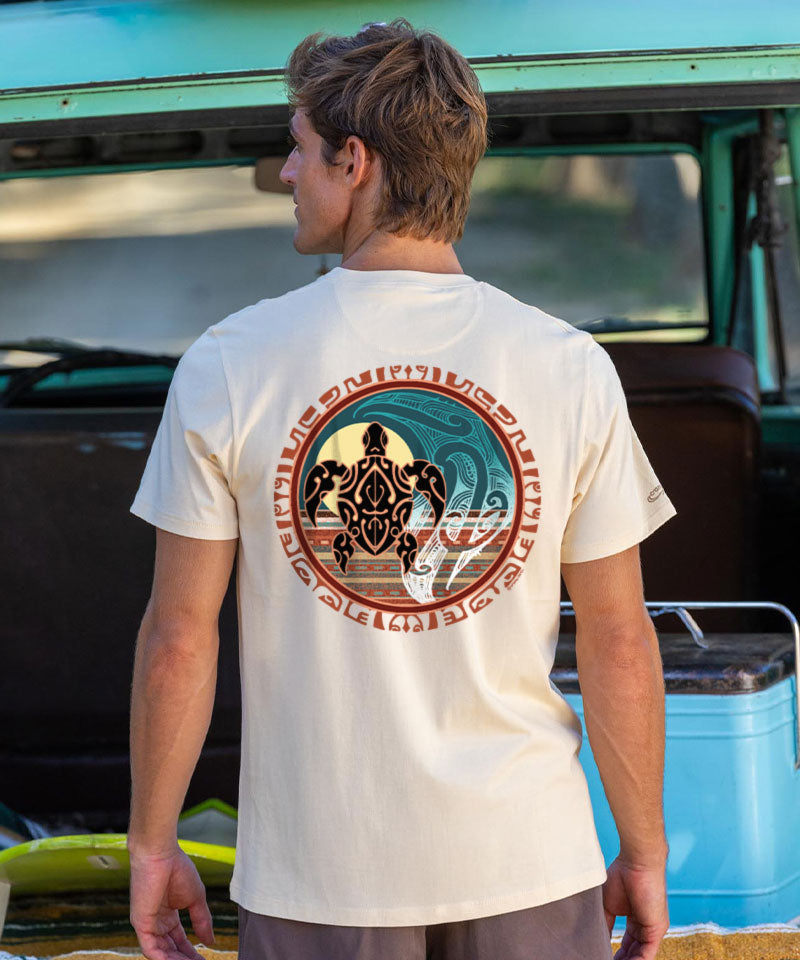 Man wearing a beige t-shirt with a logo on the back, standing in front of a vehicle