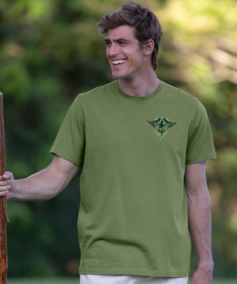 Man wearing a green t-shirt with a logo, holding a wooden stick outdoors. View 3