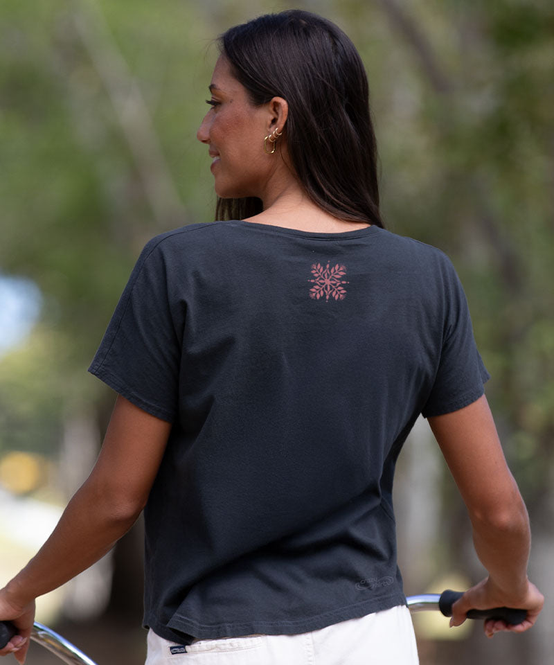Woman wearing a black t-shirt with a small logo on the back, standing outdoors. View 3