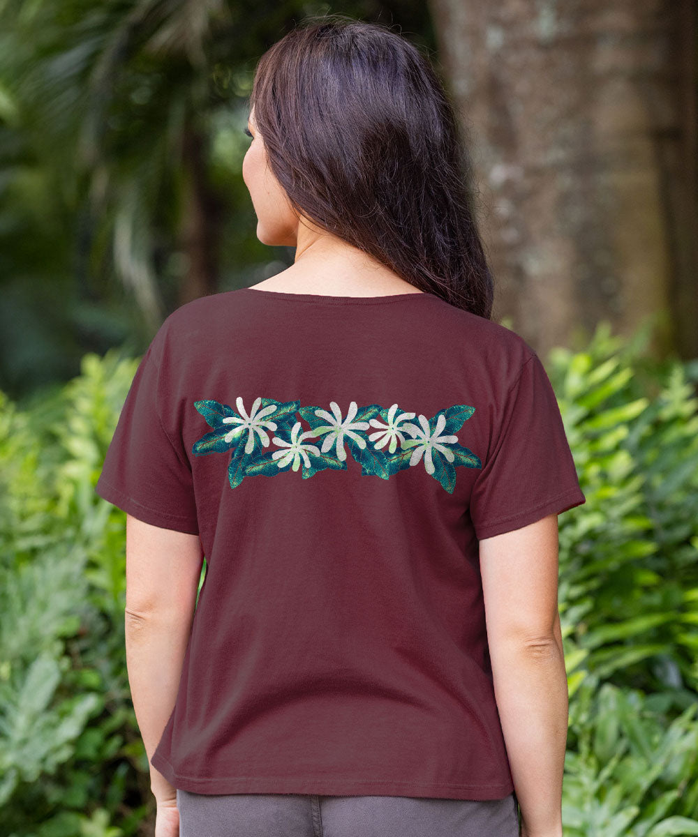A woman viewed from behind wearing a short-sleeve maroon t-shirt with a horizontal embroidered floral pattern across the upper back. The pattern features white flowers with teal centers and teal leaves. View 3
