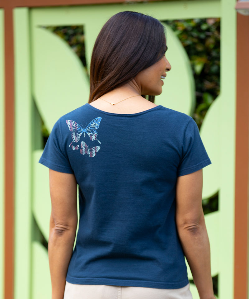 Woman wearing a blue t-shirt with butterfly designs on the back, standing in front of a green door. View 3