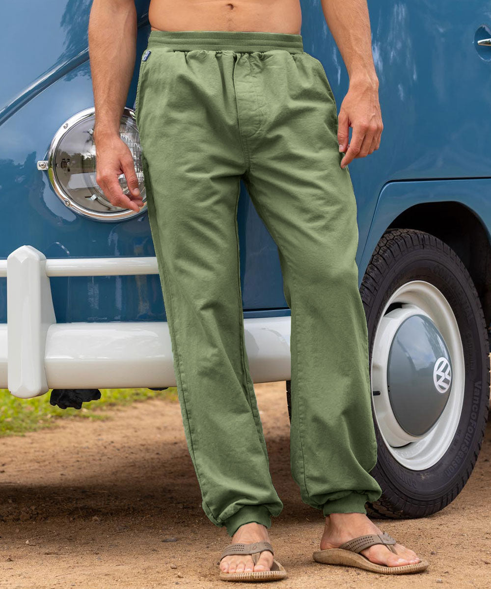 Man wearing green pants standing next to a vintage blue Volkswagen van. View 2