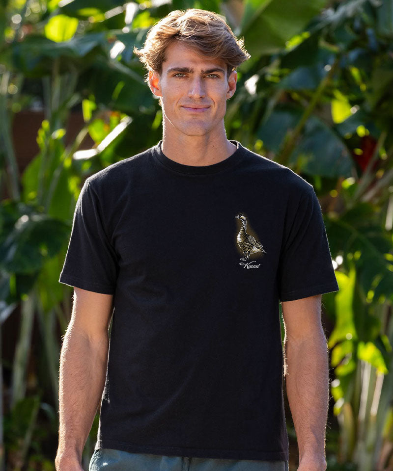 Man wearing a black t-shirt with a logo in front of green foliage View 3