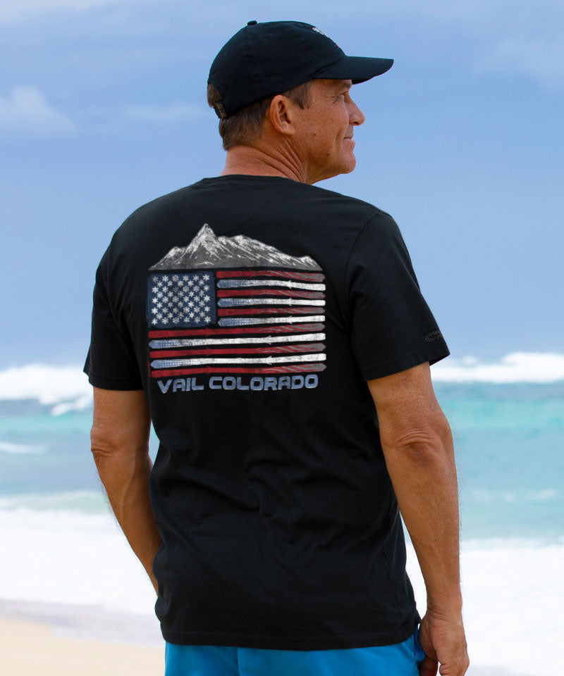 Man wearing a black t-shirt with a mountain and American flag design on the beach View 2