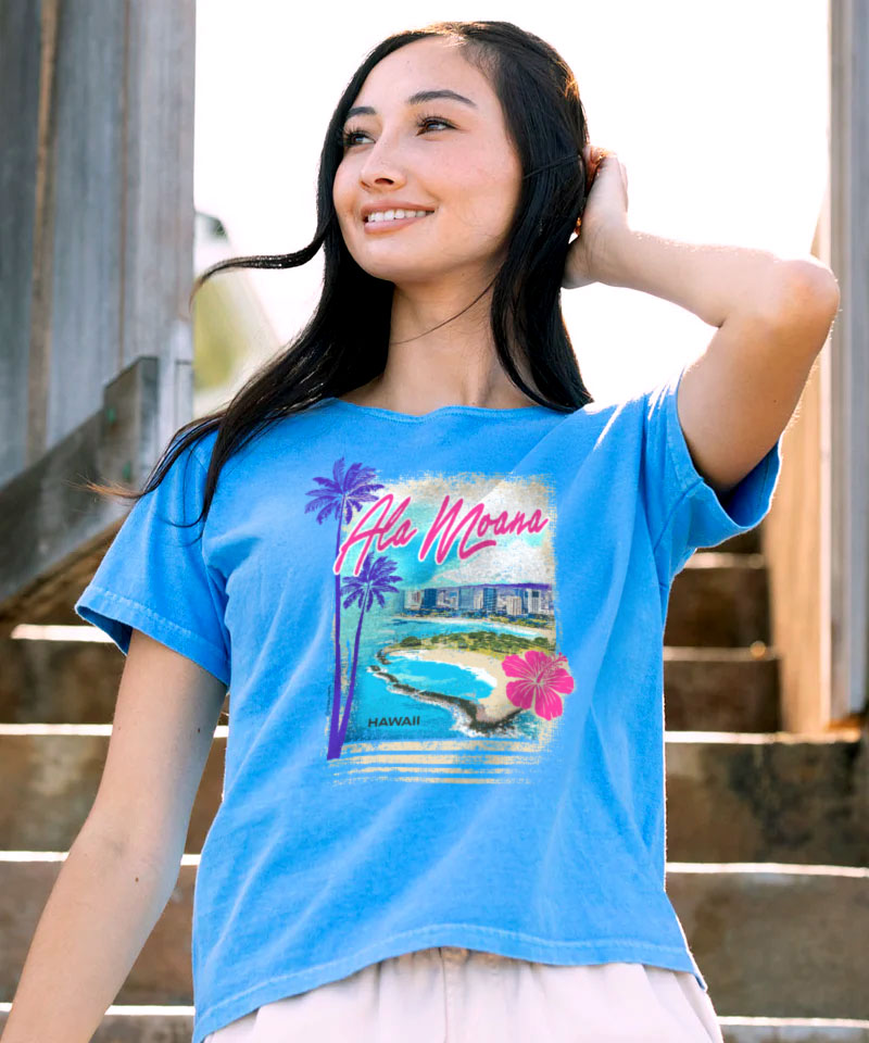 Woman wearing a blue t-shirt with a tropical graphic design outdoors. View 2