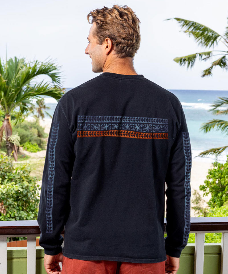 Man wearing a black long-sleeve shirt with a patterned back design, standing on a balcony with a scenic view. View 3