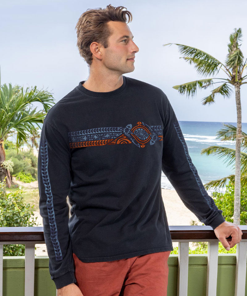 Man wearing a black long-sleeve shirt with a design, standing on a balcony with palm trees and ocean view. View 2