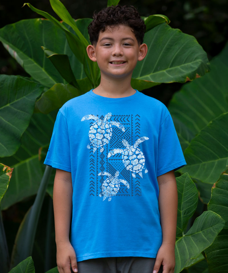 Child wearing a blue t-shirt with turtle design in front of green foliage View 2