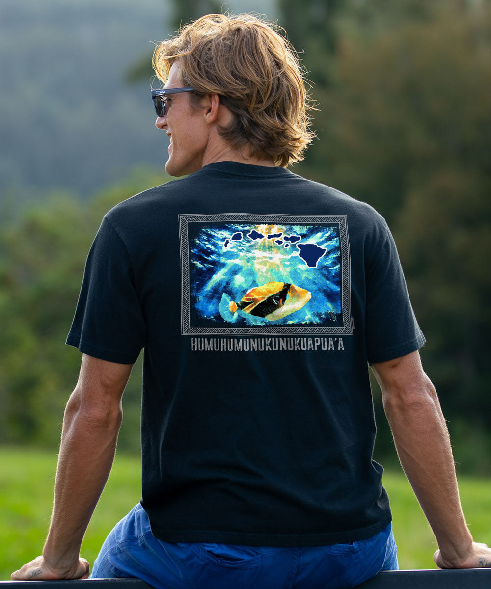 A man wearing a black t-shirt with a large graphic print on the back, photographed from behind in an outdoor setting with blurred green trees in the background. View 2