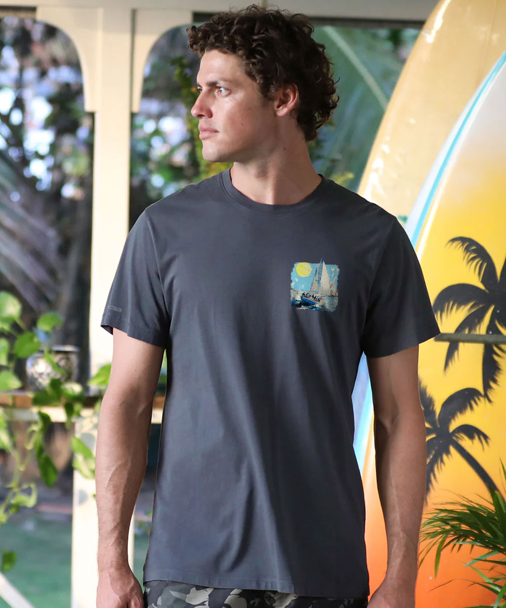 A man wearing a dark gray crewneck t-shirt with a small square graphic print on the left chest, standing in front of a tropical-themed backdrop. View 3