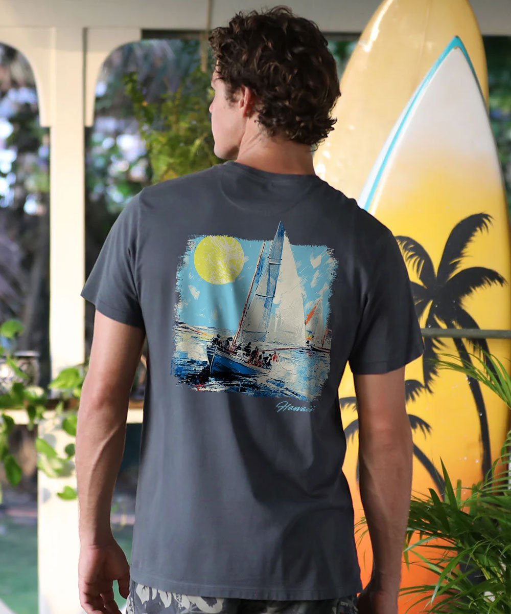 A man viewed from behind wearing a dark gray t-shirt with a colorful graphic print of a sailboat under a yellow sun on the back. He is standing in front of a yellow surfboard with palm tree silhouettes. View 2