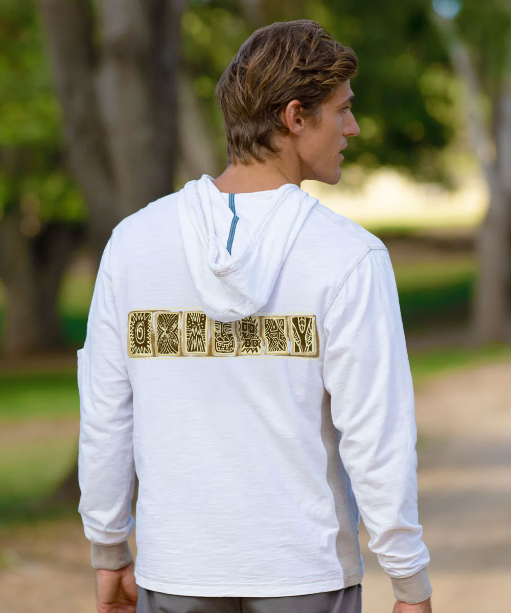 A man wearing a white long-sleeve hooded shirt with a gold-toned decorative graphic across the back, photographed outdoors in a park setting. View 3