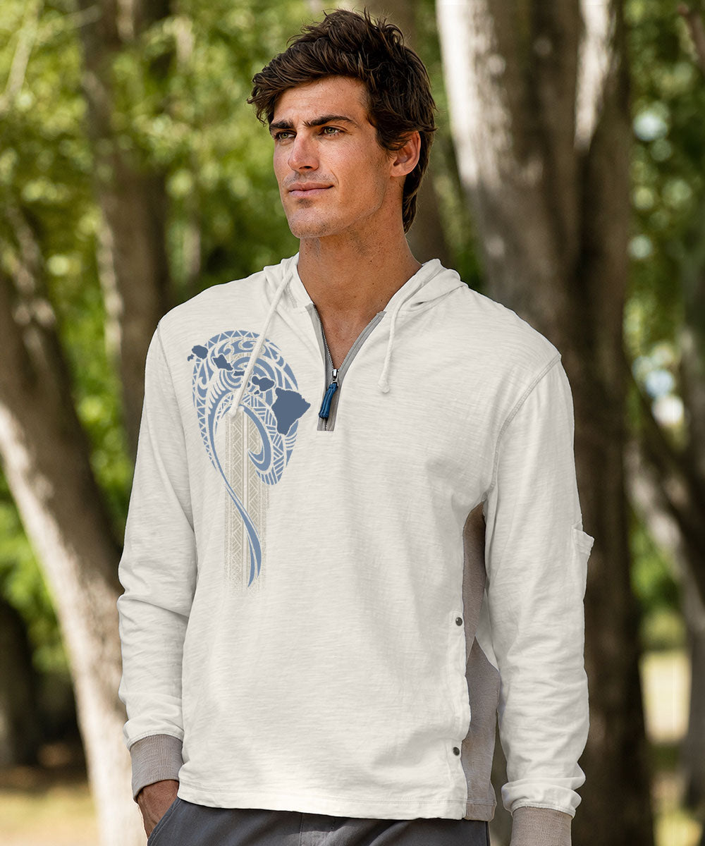 A man wearing a white quarter-zip hoodie with a blue and white graphic print on the chest, standing outdoors in front of a blurred background of trees. View 2