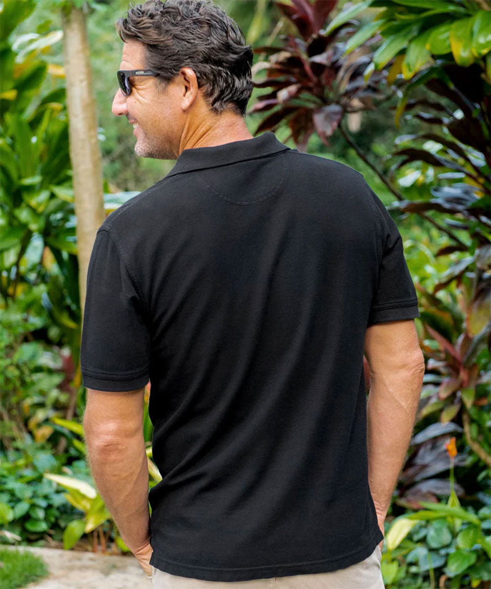 Man wearing a black polo shirt standing in a garden with greenery around View 3