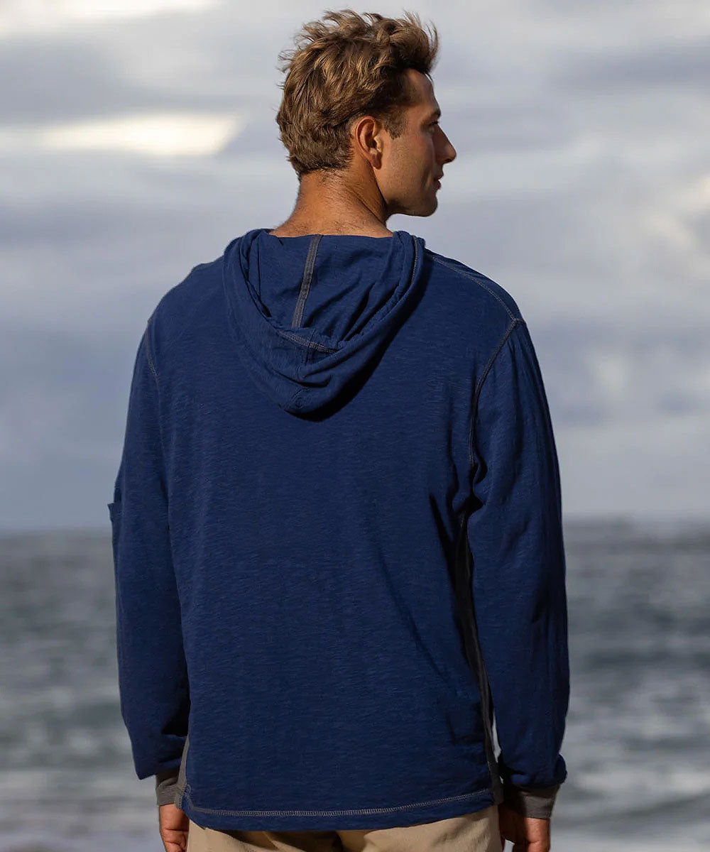 A man viewed from behind wearing a navy blue long-sleeve hooded shirt, standing outdoors with a cloudy sky and ocean in the background. View 3